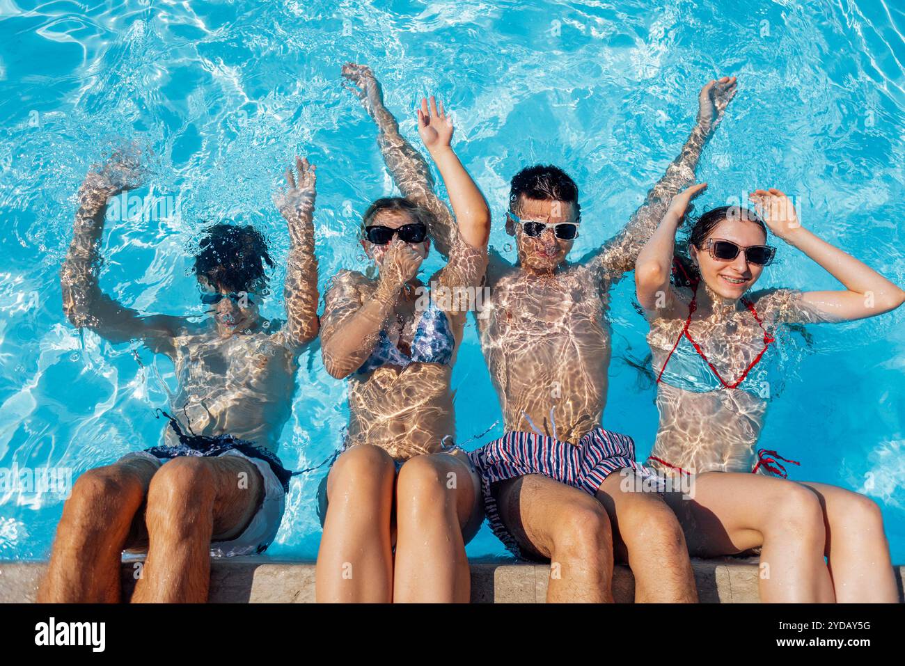 In piscina c'erano dei bei ragazzi in costume da bagno e occhiali da sole. Ragazzi e ragazze sorridenti si tuffano nell'acqua limpida. Gli adolescenti gioiosi si rilassano e.. Foto Stock