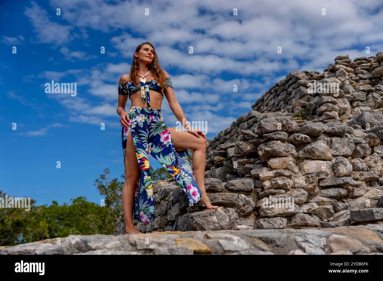 Una giovane donna radiosa esplora le rovine maya di Xcambo, la sua presenza intreccia eleganza e storia antica, sotto l'abbraccio dorato del sole caraibico Foto Stock