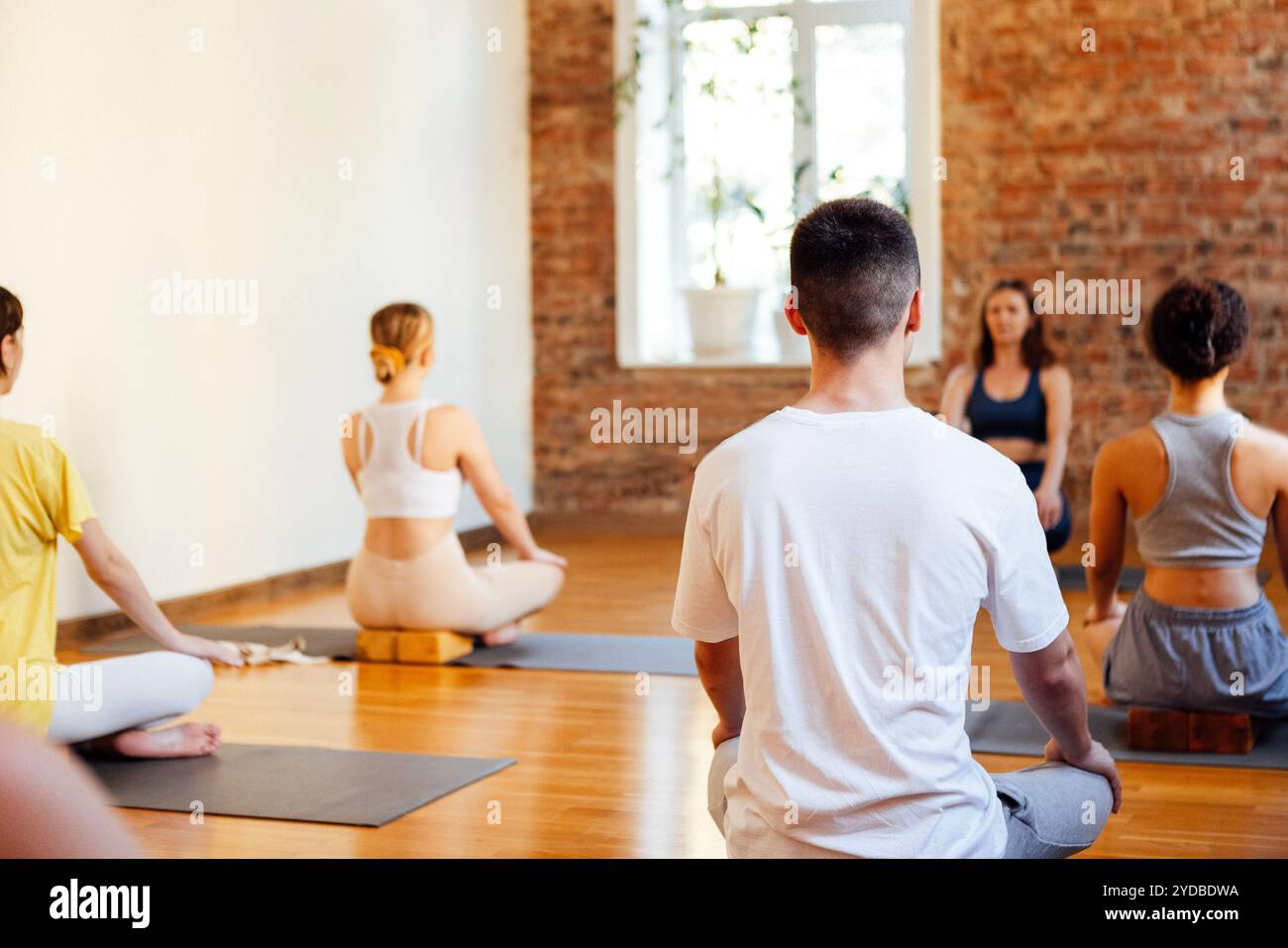 Persone atletiche di età e razze diverse praticano asana yoga con un allenatore. Giovani donne e uomini sportivi multietnici siedono cros Foto Stock