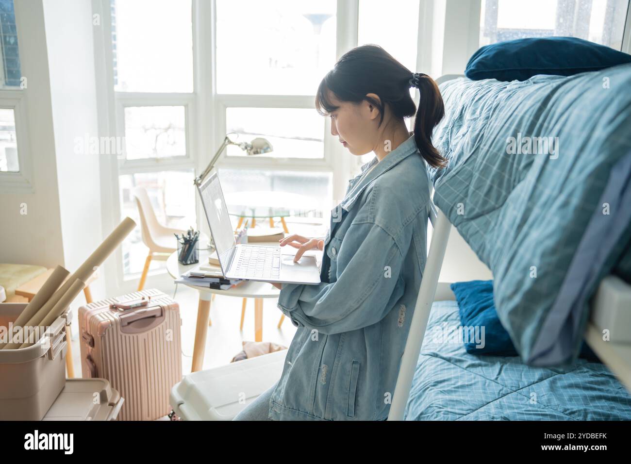 Studentessa donna asiatica seduta sul letto in dormitorio college studentâ lavoro o compiti sul portatile nel dormitorio universitario Foto Stock