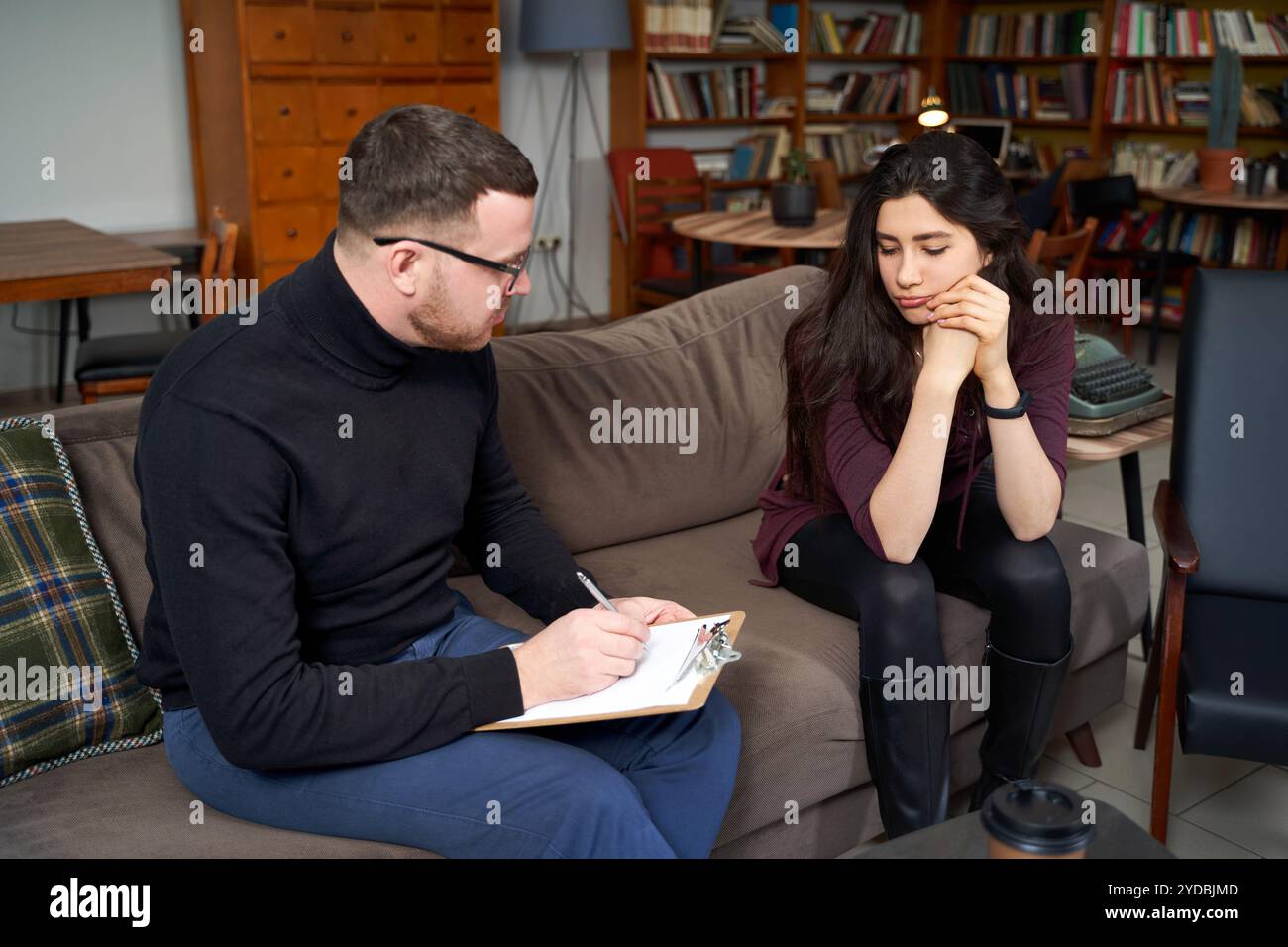 Paziente femminile che parla con il suo terapeuta che sta prendendo appunti in casa ufficio privato Foto Stock