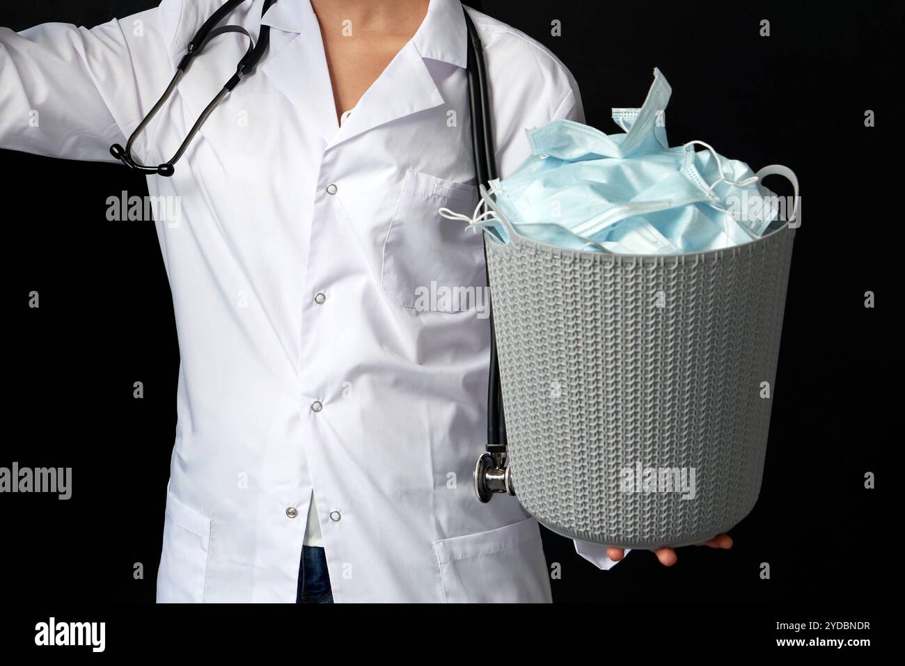 Il medico tiene il secchio pieno delle maschere facciali usate, gettandole via come simbolo di fine epidemia Foto Stock