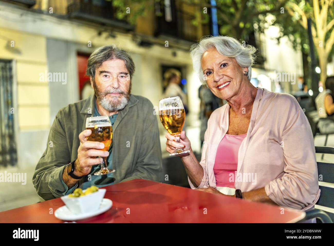 Coppia senior che brinda alla macchina fotografica con birra nella terrazza all'aperto sulla strada della città Foto Stock