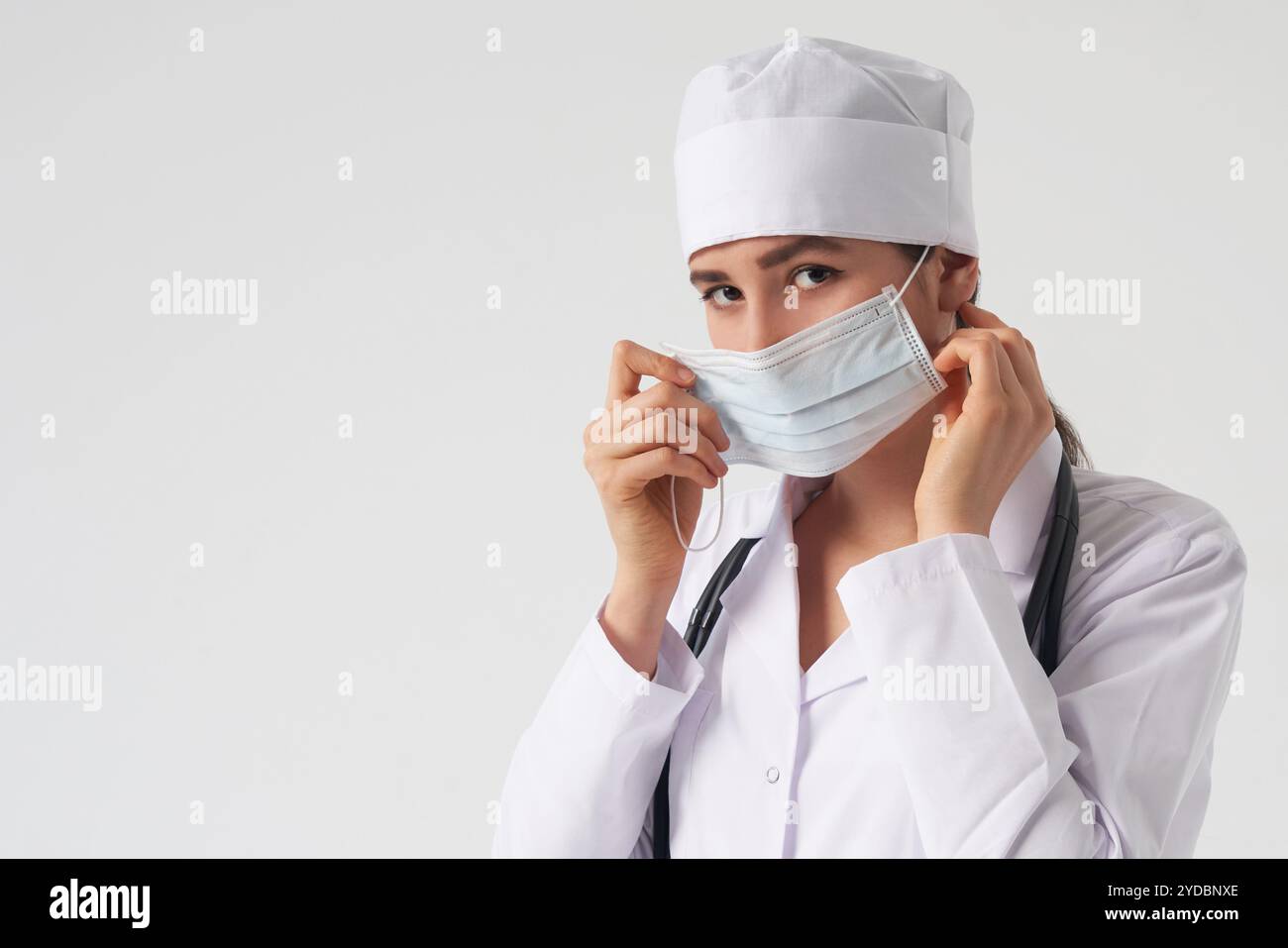 Ritratto di giovane medico femminile indossare la maschera facciale medica protettiva su sfondo bianco, spazio copia Foto Stock