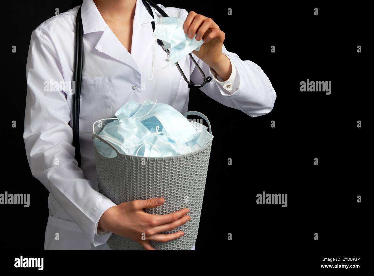 Il medico tiene il secchio pieno delle maschere facciali usate, gettandole via come simbolo di fine epidemia Foto Stock