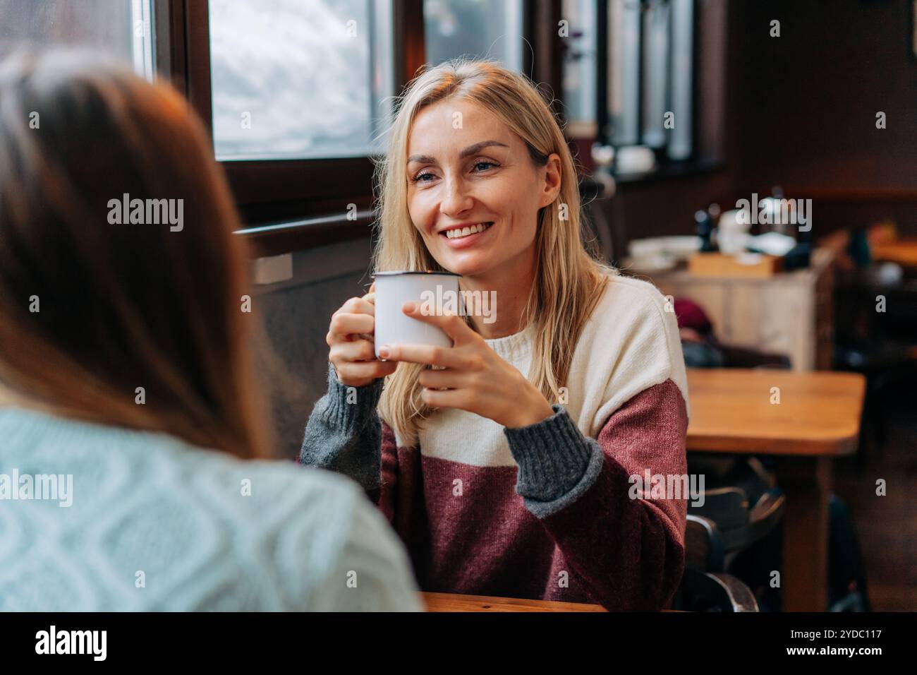 Ritratto di un'attraente bionda che chiacchiera con un amico seduto in un accogliente caffè caldo. Foto Stock