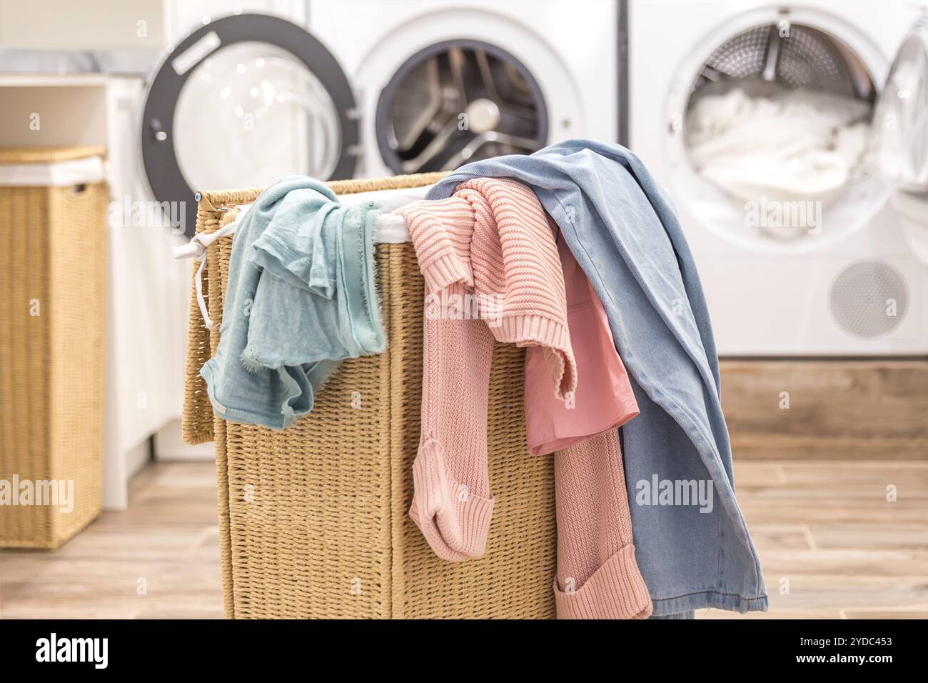 Un cesto della biancheria sporca con altri vestiti con le apparecchiature di lavaggio e di asciugatura sullo sfondo Foto Stock