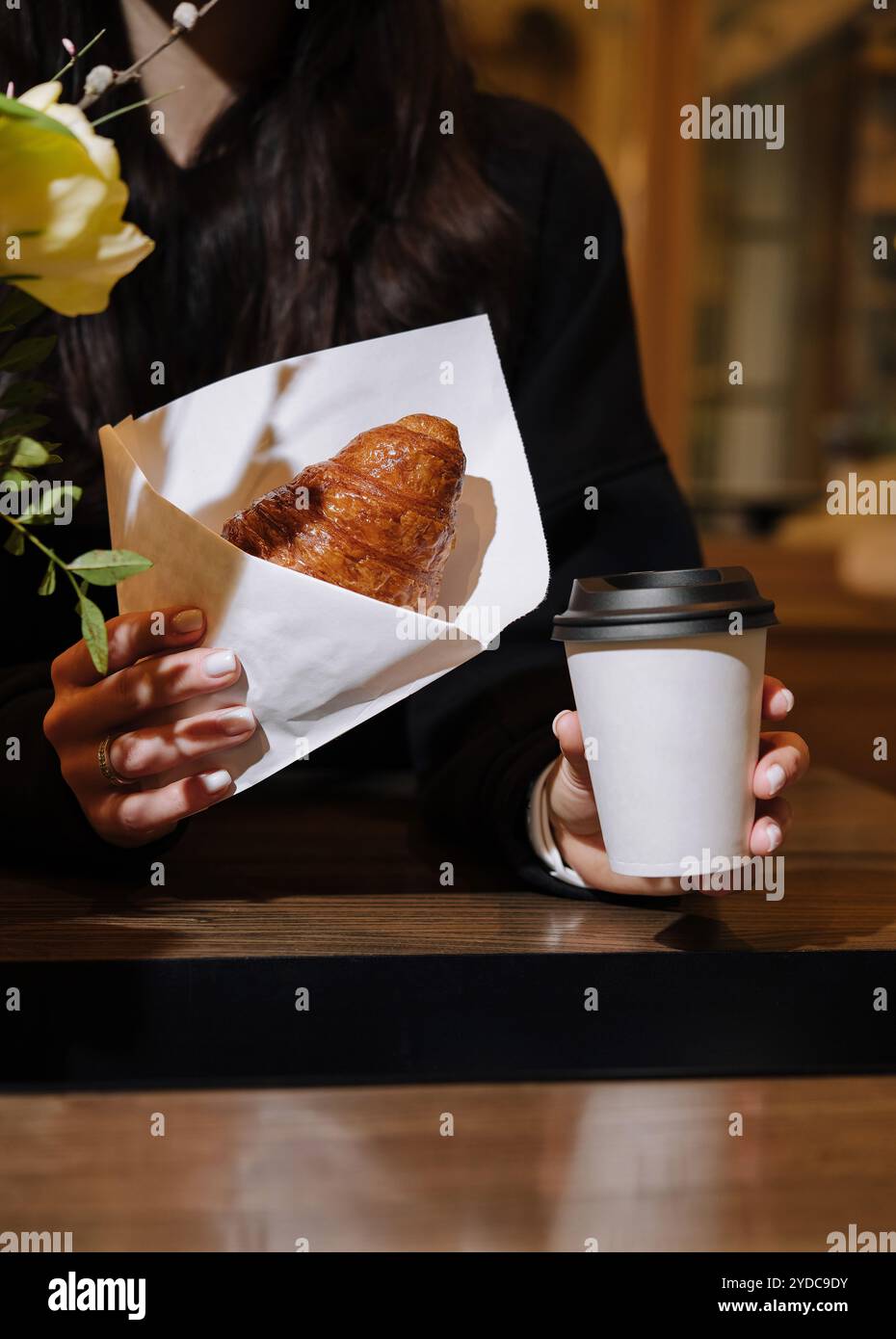 Donna che tiene in mano una tazza di caffè e un croissant in caffetteria Foto Stock