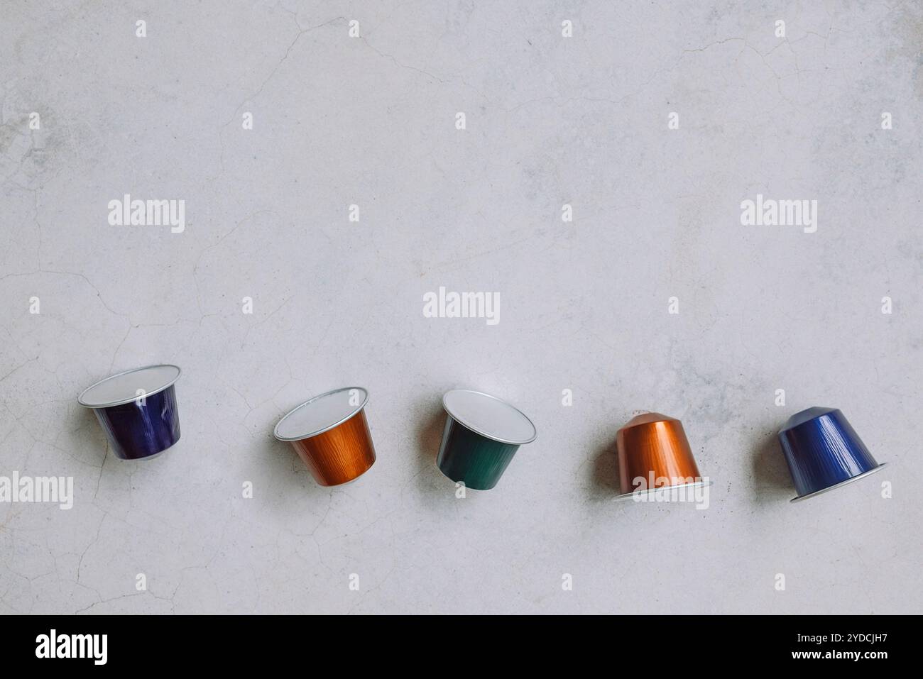 Le capsule di caffè multicolore sono sparse sulla superficie di marmo chiaro. Tonalità metallizzate brillanti. Estetica moderna e minimalista. Copia spazio Foto Stock