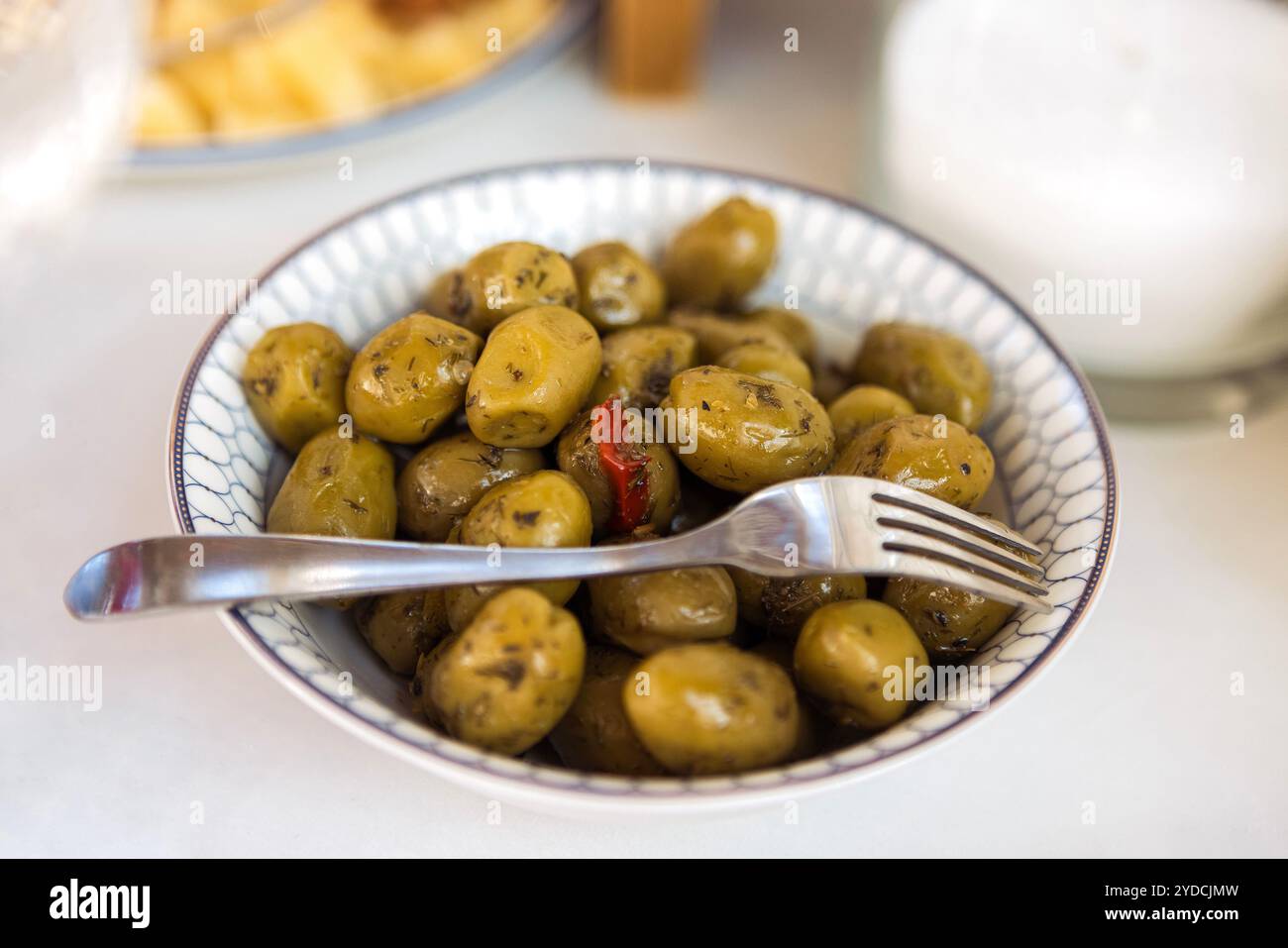 Olive verdi profumate con spezie. Primo piano di un piatto con deliziosi frutti dell'olivo e delle erbe su una tavola bianca. Gustosi spuntini vegani Foto Stock