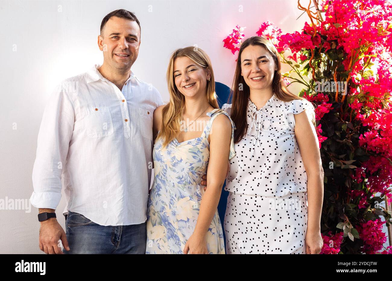 Un'adolescente carina e i suoi genitori in abiti eleganti sorridono e si mettono in posa. Una ragazza gioiosa, suo padre e sua mamma si abbracciano a una riunione festosa. Un uomo e una donna Foto Stock