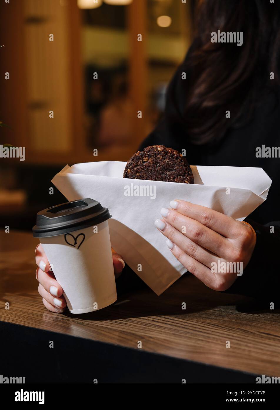 Donna che tiene in mano una tazza di caffè e biscotti d'avena in caffetteria Foto Stock