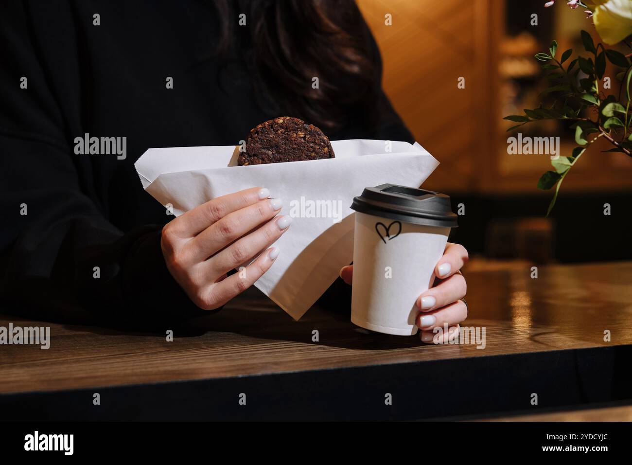 Donna che tiene in mano una tazza di caffè e biscotti d'avena in caffetteria Foto Stock