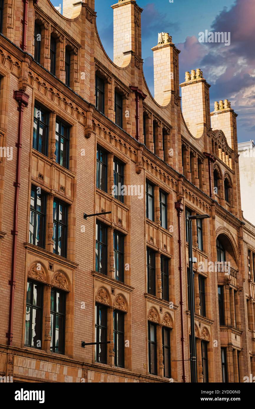 Un'immagine a basso angolo di un edificio in mattoni con dettagli ornamentali, numerose finestre e camini multipli, catturati sotto un cielo nuvoloso a Manchester, Regno Unito. Foto Stock