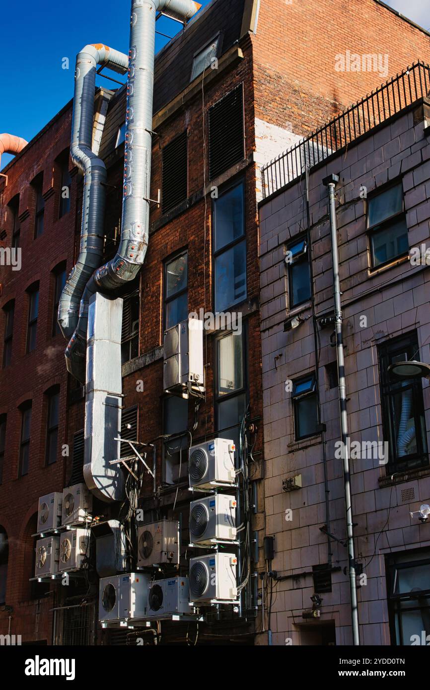 Un primo piano di due edifici in mattoni con un grande albero di ventilazione in argento e diverse unità di aria condizionata bianche sul lato dell'edificio a Manch Foto Stock