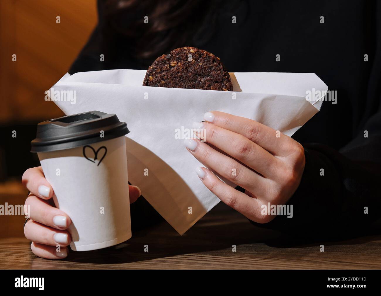 Donna che tiene in mano una tazza di caffè e biscotti d'avena in caffetteria Foto Stock