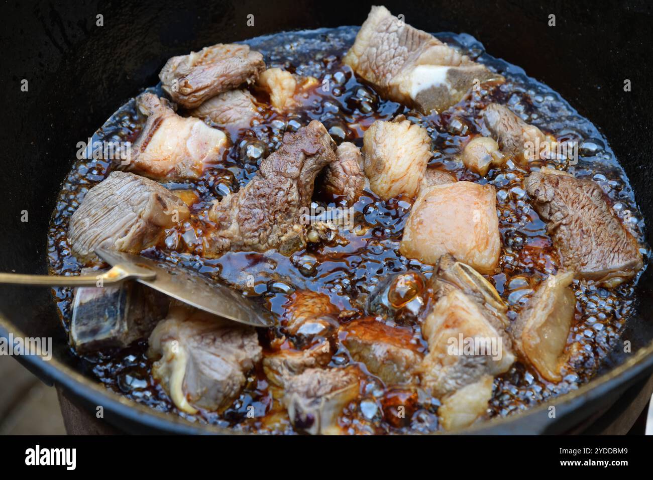 Il processo di cottura del pilaf uzbeko. La carne di manzo viene fritta nell'olio in un calderone di ghisa. Cucina tradizionale uzbeka orientale, pilaf o plov con pezzi grandi Foto Stock