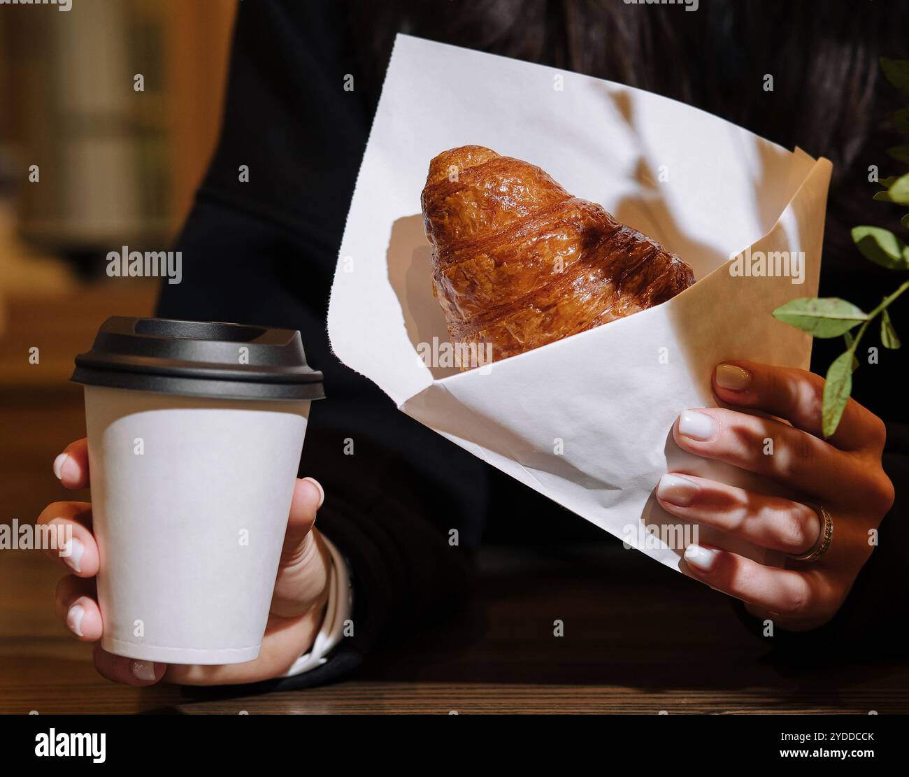 Donna che tiene in mano una tazza di caffè e un croissant in caffetteria Foto Stock