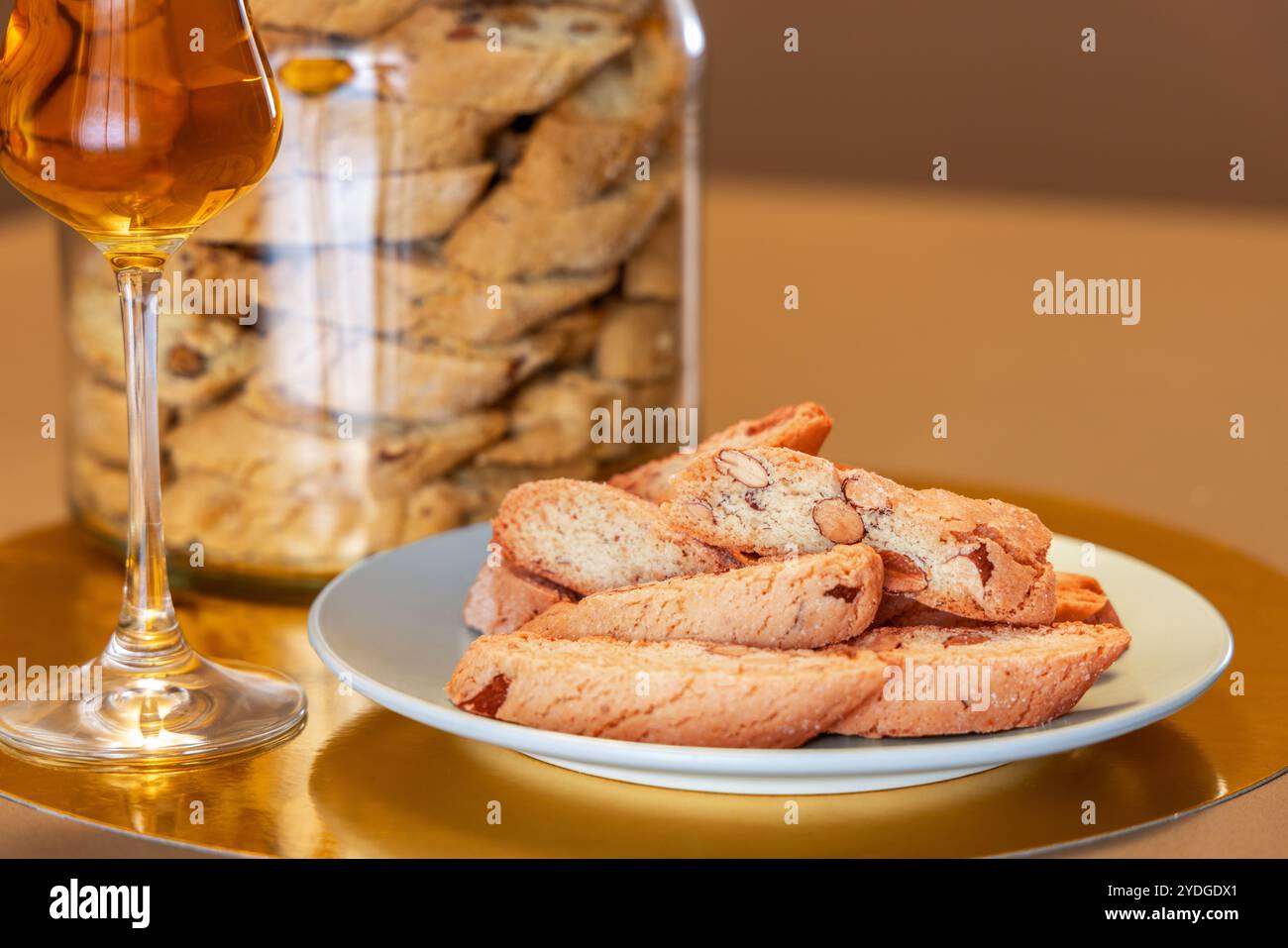 Cantucci di mandorle croccanti serviti con vino da dessert Vin Santo, che offre un classico abbinamento italiano, splendidamente adagiato su uno sfondo dorato e beige Foto Stock