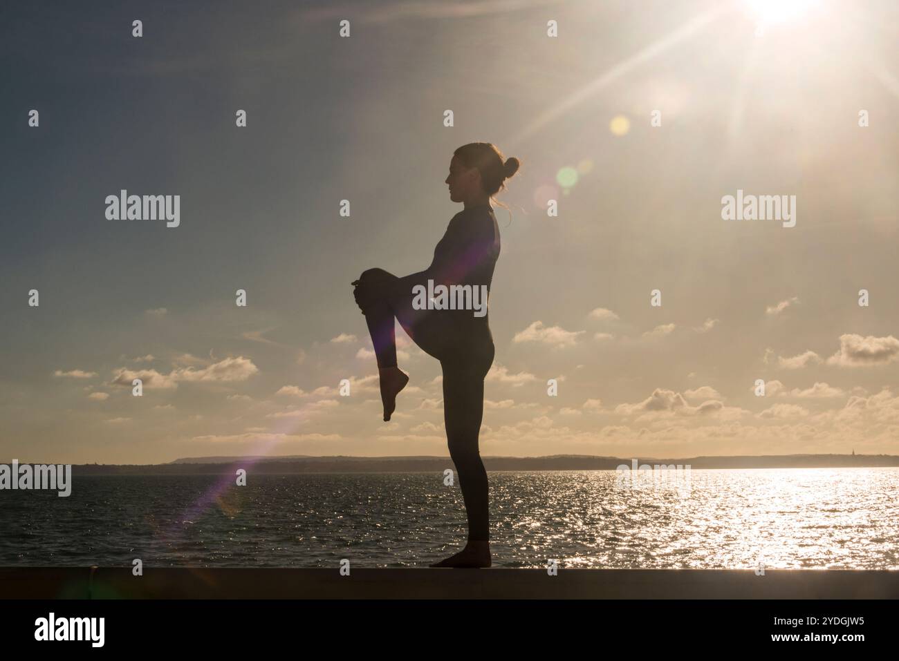 Silhoutte di una donna sportiva che si allunga una gamba all'aperto in riva al mare Foto Stock
