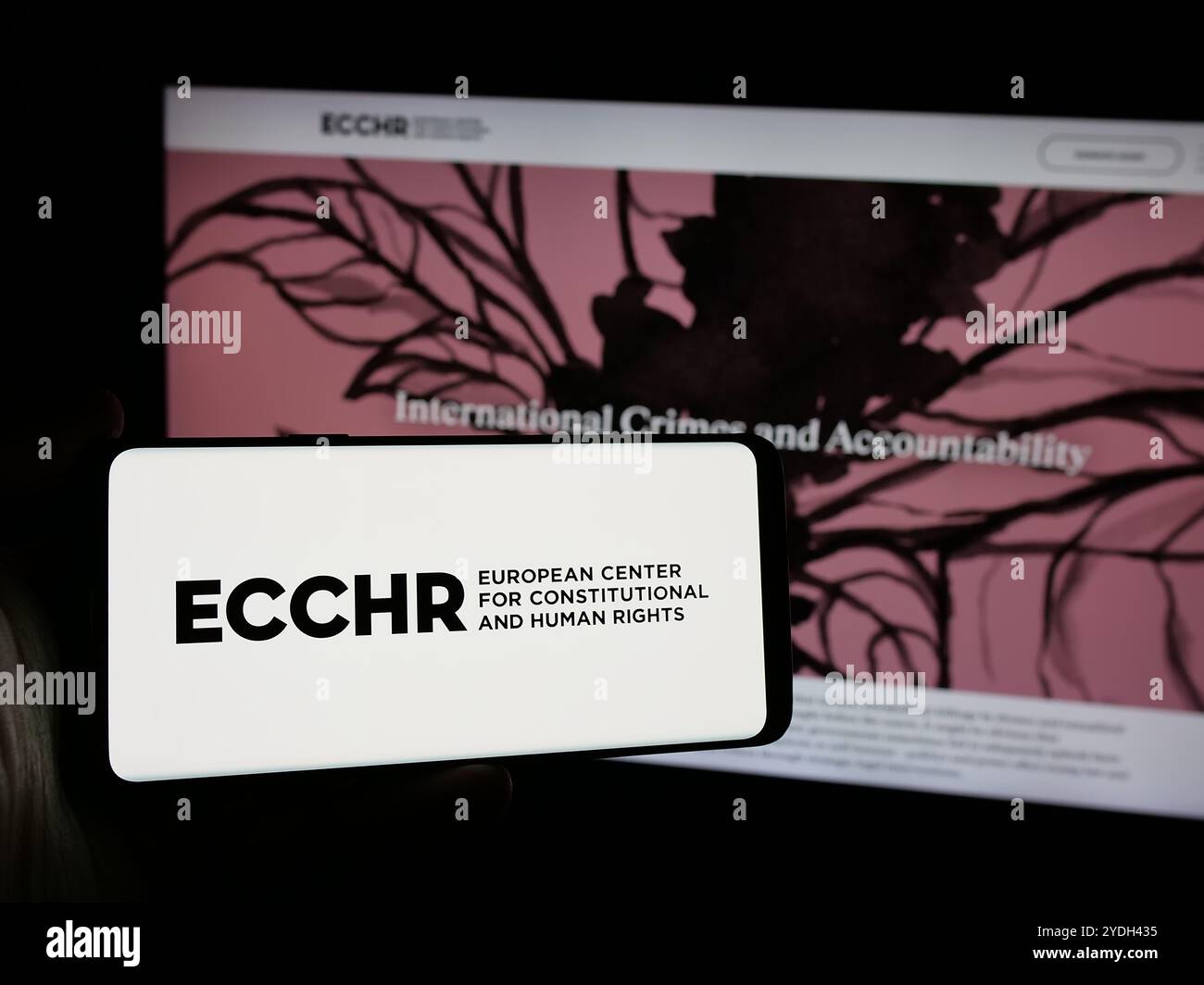 Persona che possiede uno smartphone con il logo dell’organizzazione per i diritti umani ECCHR sullo schermo di fronte al sito web. Mettere a fuoco il display del telefono. Foto Stock