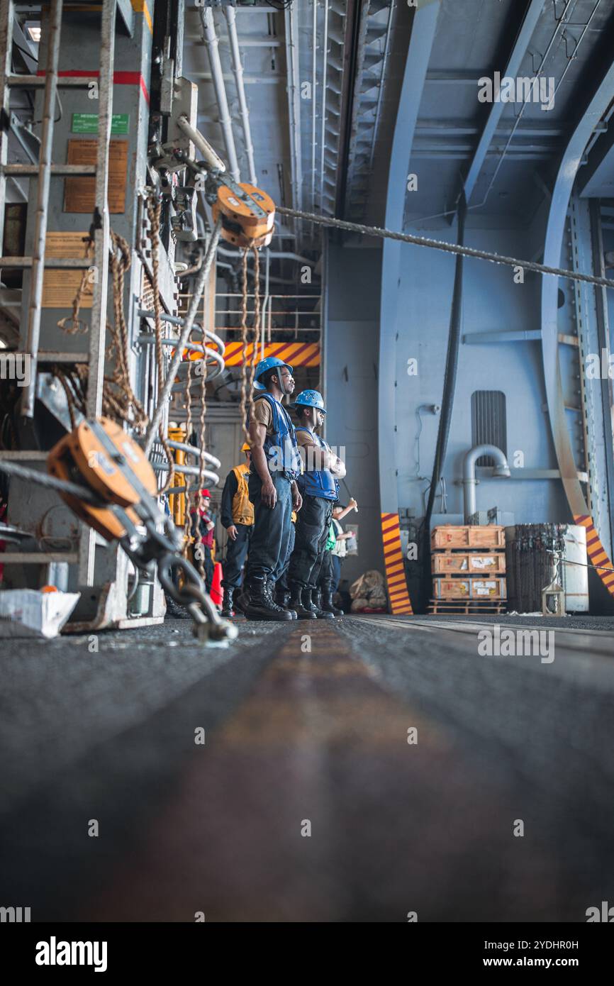 I marinai assegnati alla divisione avanzata del reparto di coperta sono in attesa di ricevere rifornimenti nella baia degli hangar a bordo della portaerei classe Nimitz USS George Washington (CVN 73) durante un rifornimento in mare con la nave classe Lewis e Clark USNS Cesar Chavez (T-AKE 14) mentre era in corso nell'Oceano Pacifico, il 25 ottobre 2024. George Washington è la prima portaerei in servizio in avanti della 7th Fleet, un simbolo di lunga data dell’impegno degli Stati Uniti a mantenere una regione indo-pacifica libera e aperta, mentre opera a fianco degli Alleati e dei partner in tutti i larghi della Marina degli Stati Uniti Foto Stock