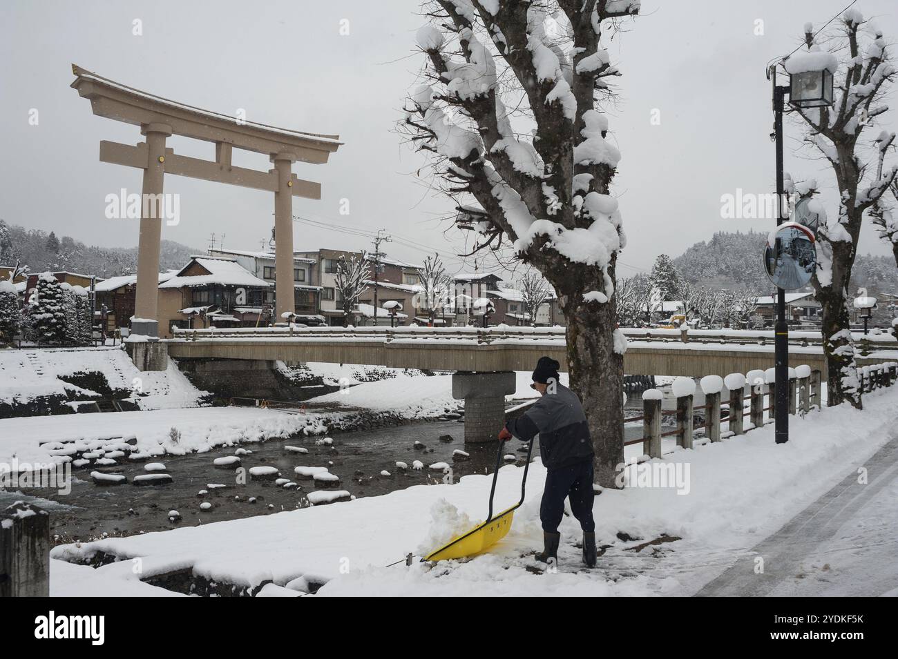 28.12.2017, Takayama, Gifu, Giappone, Asia, un uomo spalanca la neve su una strada accanto al ponte Miyamae Bashi, a un'estremità della quale si trova una grande porta torii Foto Stock