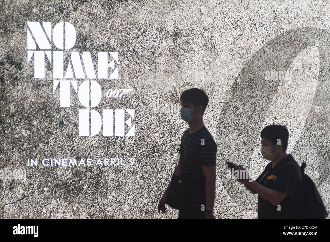 12.03.2020, Singapore, Repubblica di Singapore, Asia, due persone passano davanti a uno spazio pubblicitario per il nuovo film di James Bond indossando una maschera per la prote Foto Stock
