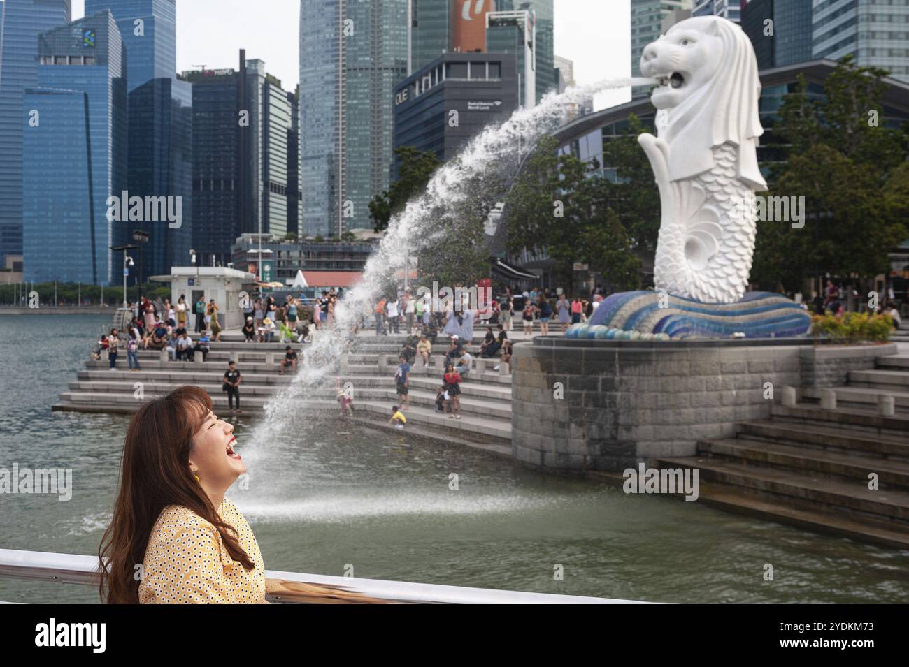 25.07.2019, Singapore, Repubblica di Singapore, Asia, Un turista posa per le foto al Merlion Park sulle rive del fiume Singapore con gli affari d Foto Stock