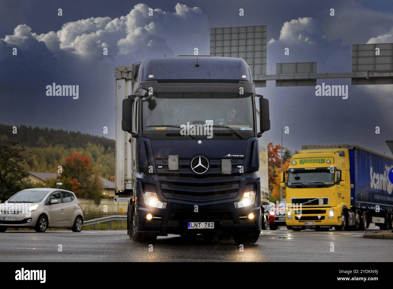 Incrocio stradale con la svolta nera Mercedes-Benz Actros per il trasporto merci. Pioggia, fari luminosi, nuvole scure. Salo, Finlandia. Setto Foto Stock