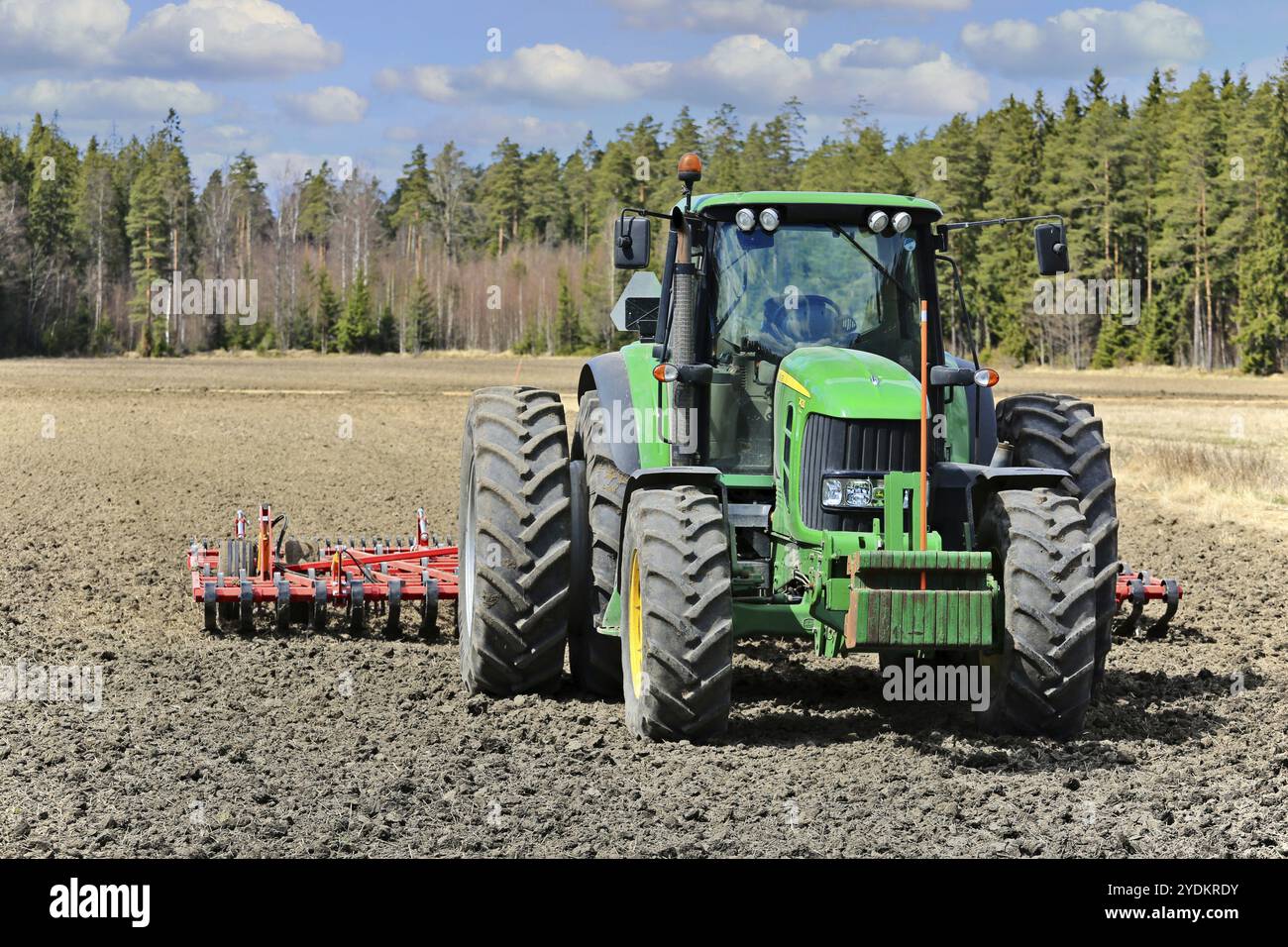 Trattore John Deere 7430 davanti all'aratro erpico su campi coltivati in una splendida giornata di primavera. Salo, Finlandia. 13 maggio 2017 Foto Stock