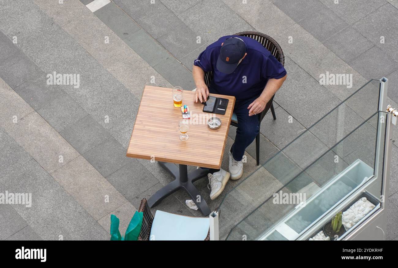 Vista dall'alto di un uomo al tavolo con birra e telefono cellulare al bar, in Spagna. Foto Stock