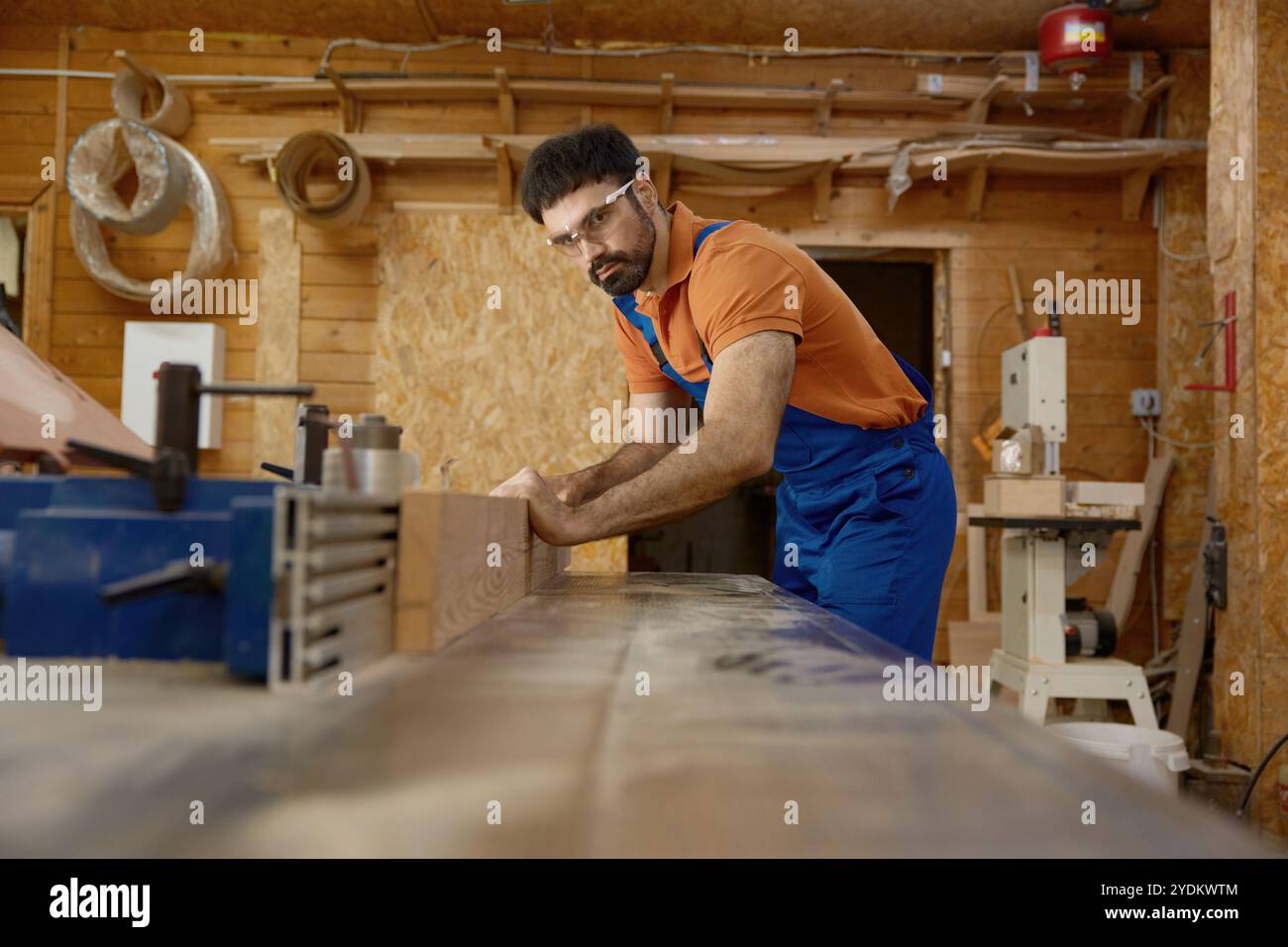 Uomo falegname professionista che indossa abbigliamento da lavoro che lavora con la tavola di legno Foto Stock