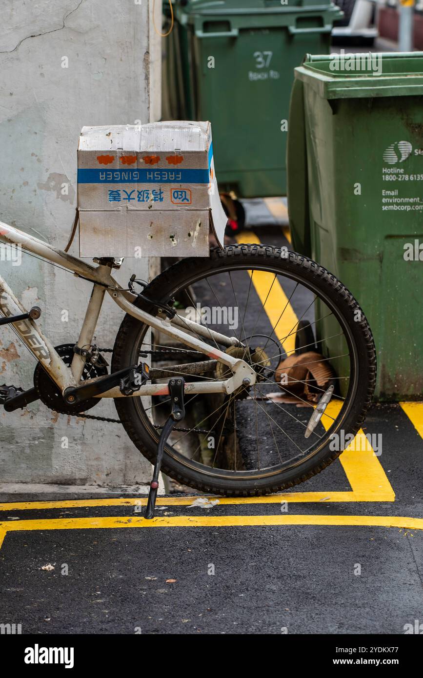 Immagine parziale di una bicicletta parcheggiata in una corsia di Singapore o in una corsia posteriore con una scatola di cartone che copre il sedile Foto Stock