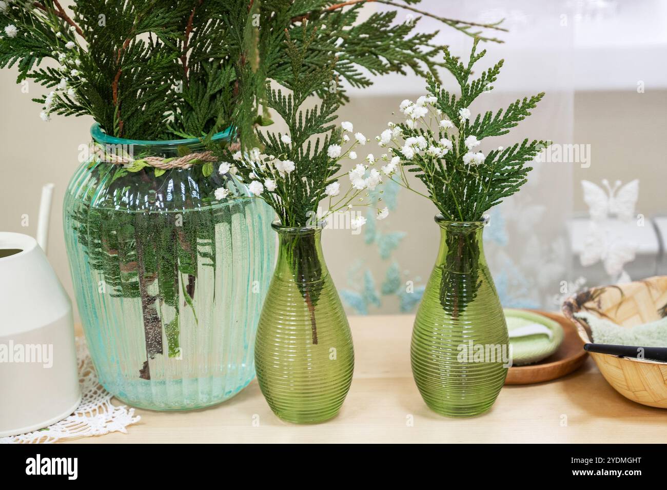 Un tavolo con vasi di vetro verde pieni di felci e fiori bianchi, che creano un arredamento fresco e naturale. Foto Stock