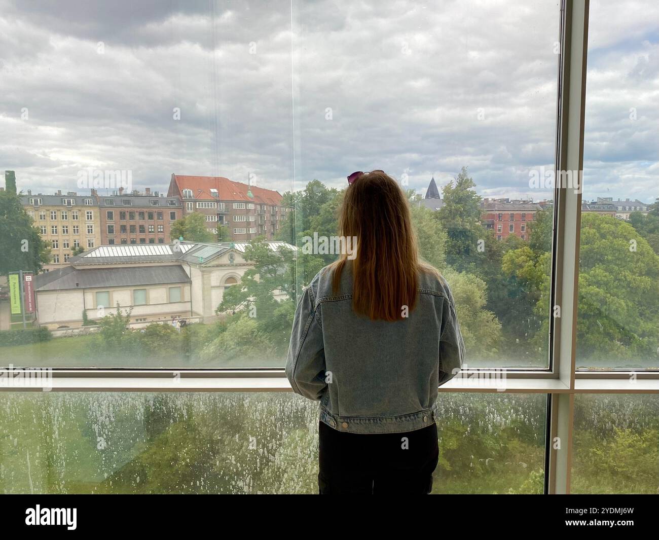 Copenaghen, Danimarca - 9 luglio 2022: Momento contemplativo: Donna che guarda il paesaggio urbano attraverso la grande finestra alla Galleria Nazionale di Danimarca Foto Stock