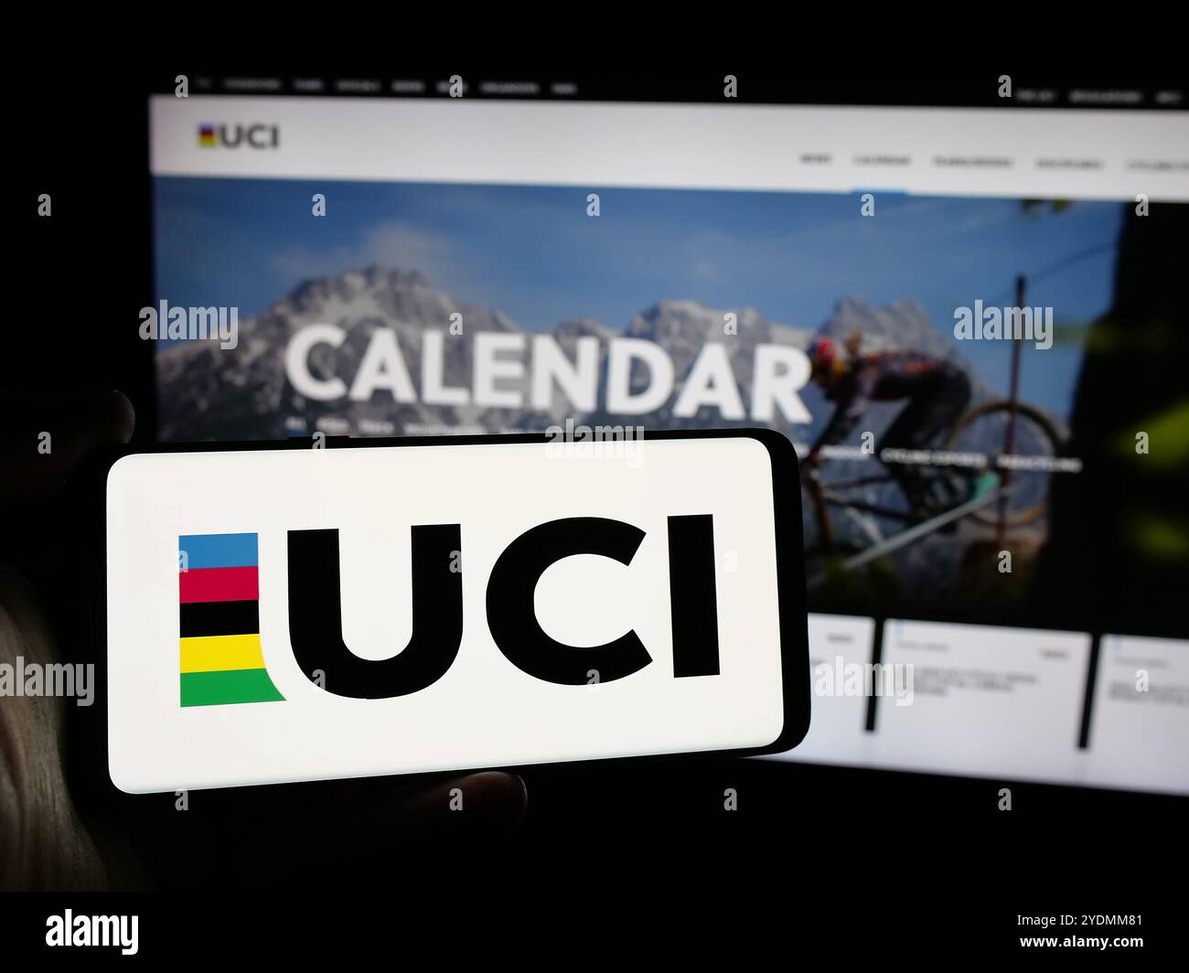 Persona che detiene un cellulare con il logo dell’Union Cycliste Internationale (UCI) sullo schermo di fronte alla pagina web. Mettere a fuoco il display del telefono. Foto Stock