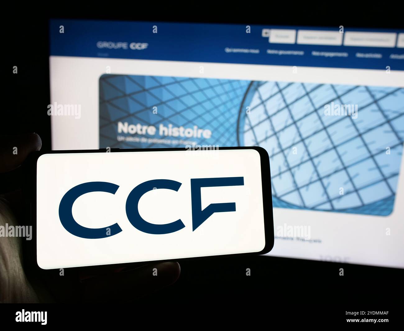 Persona che detiene un cellulare con il logo della società Credit Commercial de France (CCF) sullo schermo di fronte alla pagina Web dell'azienda. Mettere a fuoco il display del telefono. Foto Stock