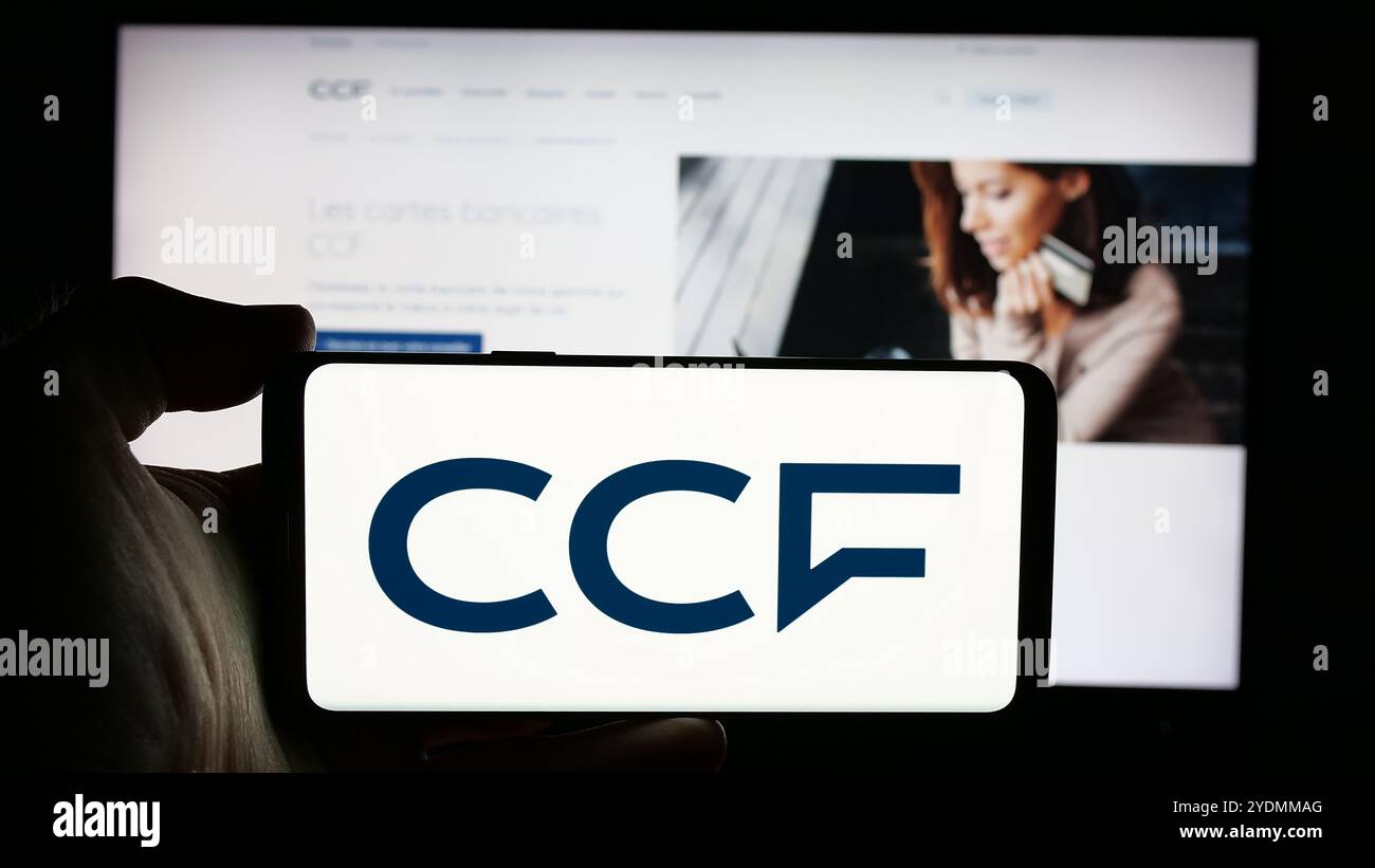 Persona che detiene un telefono cellulare con il logo della società Credit Commercial de France (CCF) sullo schermo davanti alla pagina Web. Mettere a fuoco il display del telefono. Foto Stock