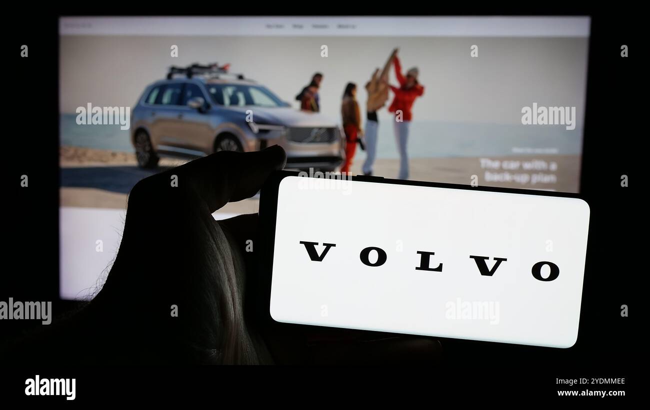 Persona che possiede uno smartphone con il logo dell'azienda automobilistica svedese Volvo Car AB sullo schermo di fronte al sito Web. Mettere a fuoco il display del telefono. Foto Stock