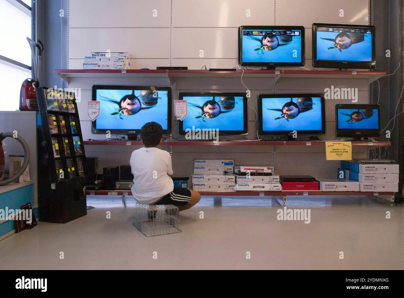 In der TV-Abteilung eines Supermarktes guckt ein kind fasziniert Fernsehen. Foto Stock