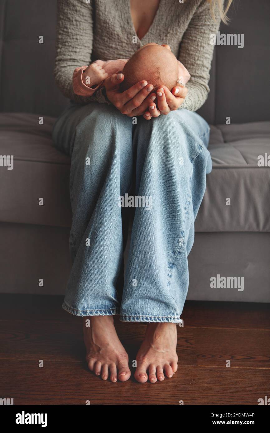 Primo piano la madre culla e dondola delicatamente il neonato tra le braccia. Concentratevi sulle mani che trattengono il bambino, catturando un momento tenero e intimo di cura materna e. Foto Stock