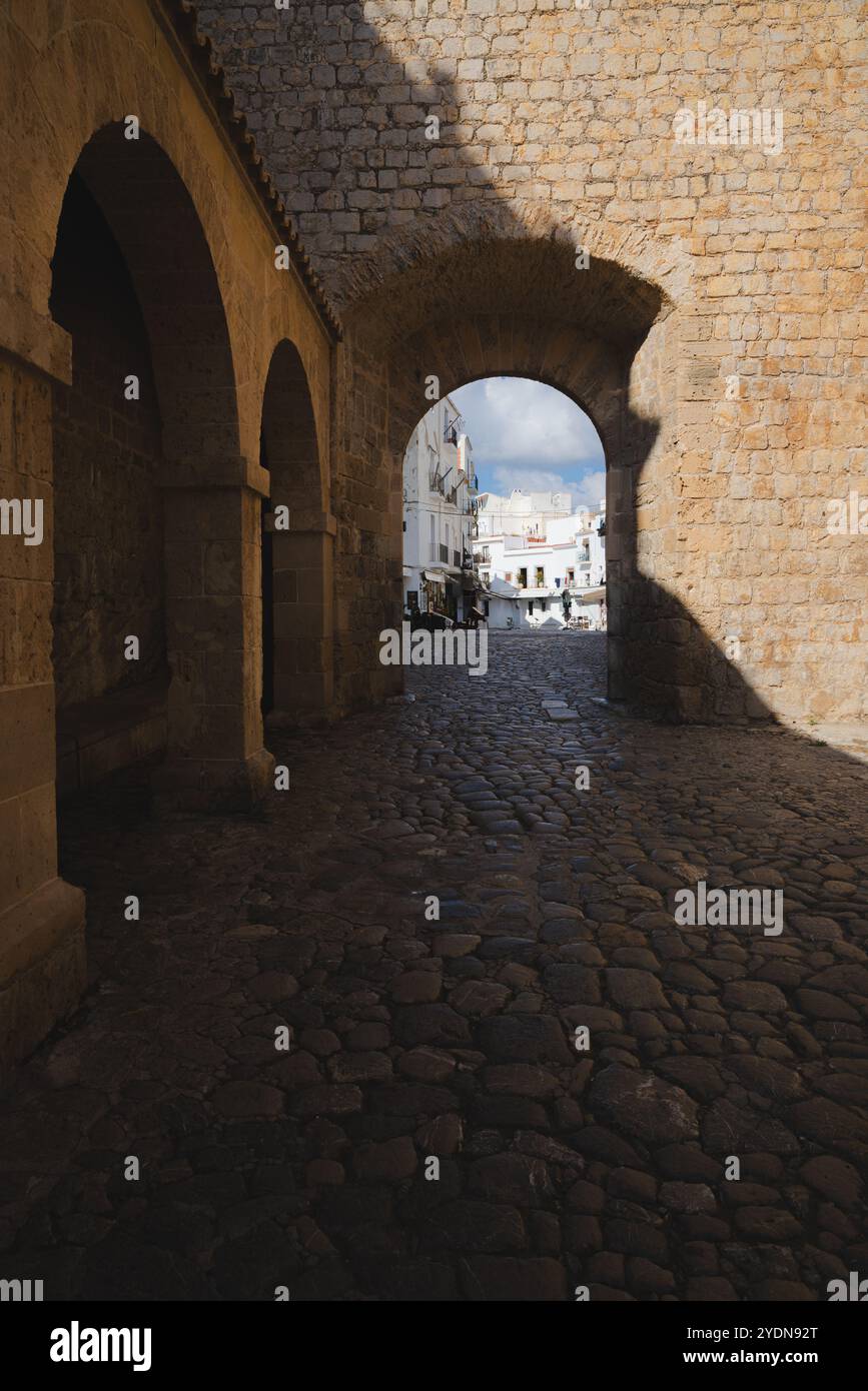 Affascinante arcata in pietra che conduce alle strade acciottolate della città vecchia di Ibiza, catturando la bellezza rustica e il fascino storico di questa gemma mediterranea. Foto Stock