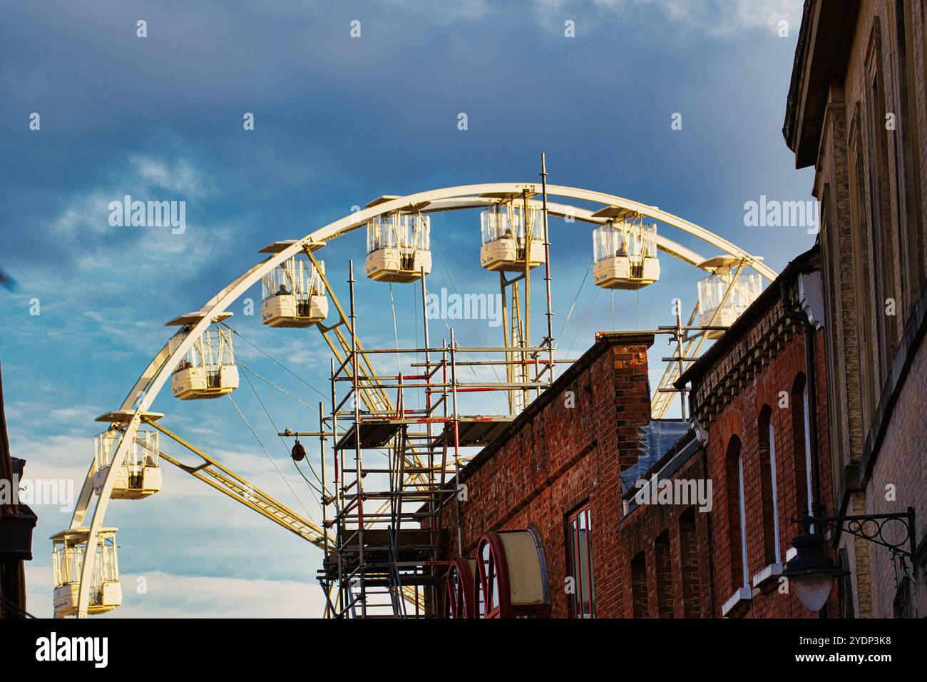 Una ruota panoramica parzialmente costruita è posizionata sullo sfondo, con impalcature visibili e diverse cabine vuote. In primo piano, due mattoni Foto Stock