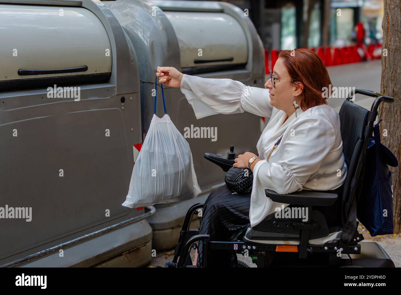 Donna in sedia a rotelle che deposita la spazzatura nel cestino urbano Foto Stock