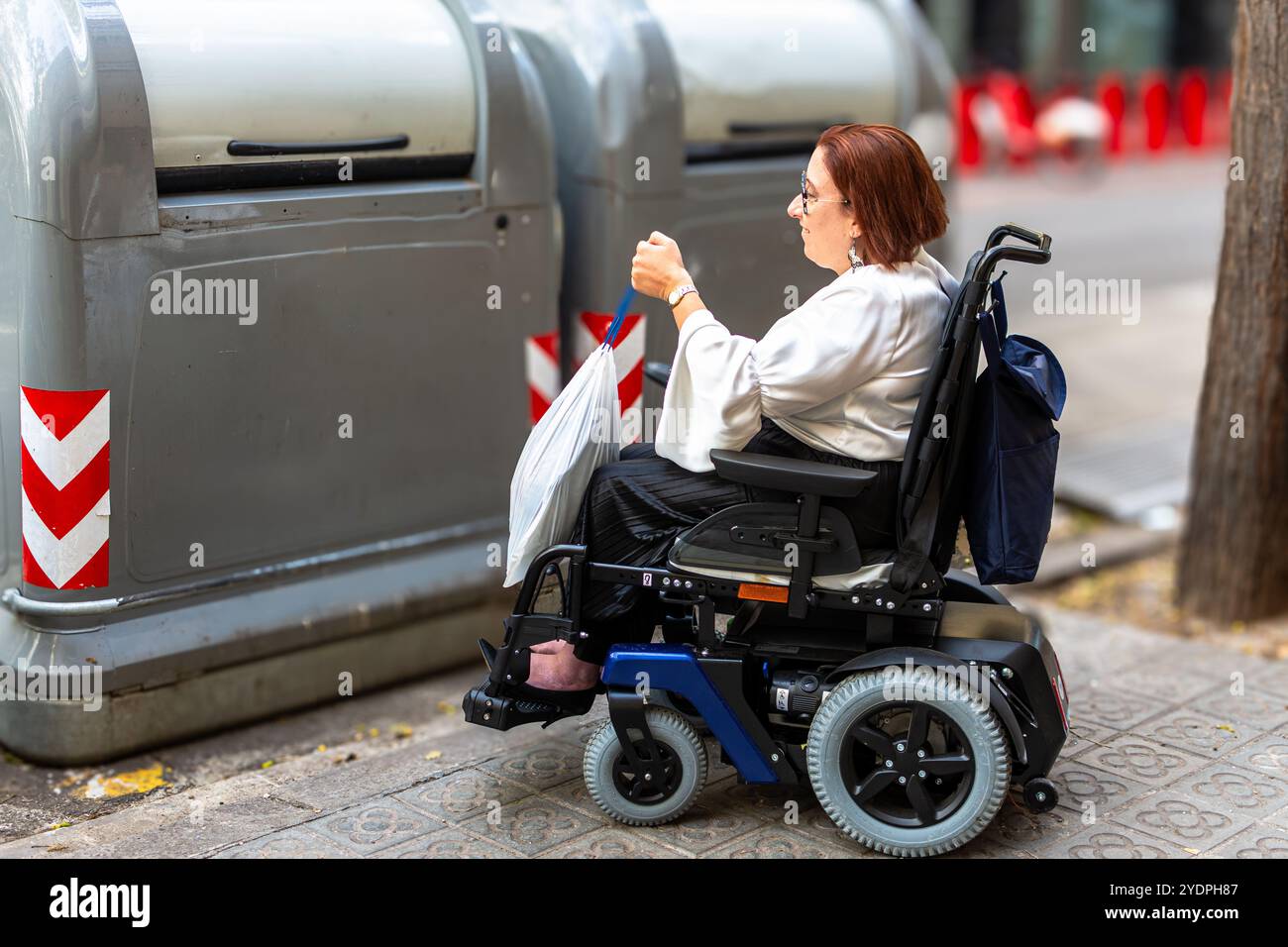 Utente con sedia a rotelle che deposita il cestino nel cestino di riciclaggio accessibile con sedia a rotelle Foto Stock