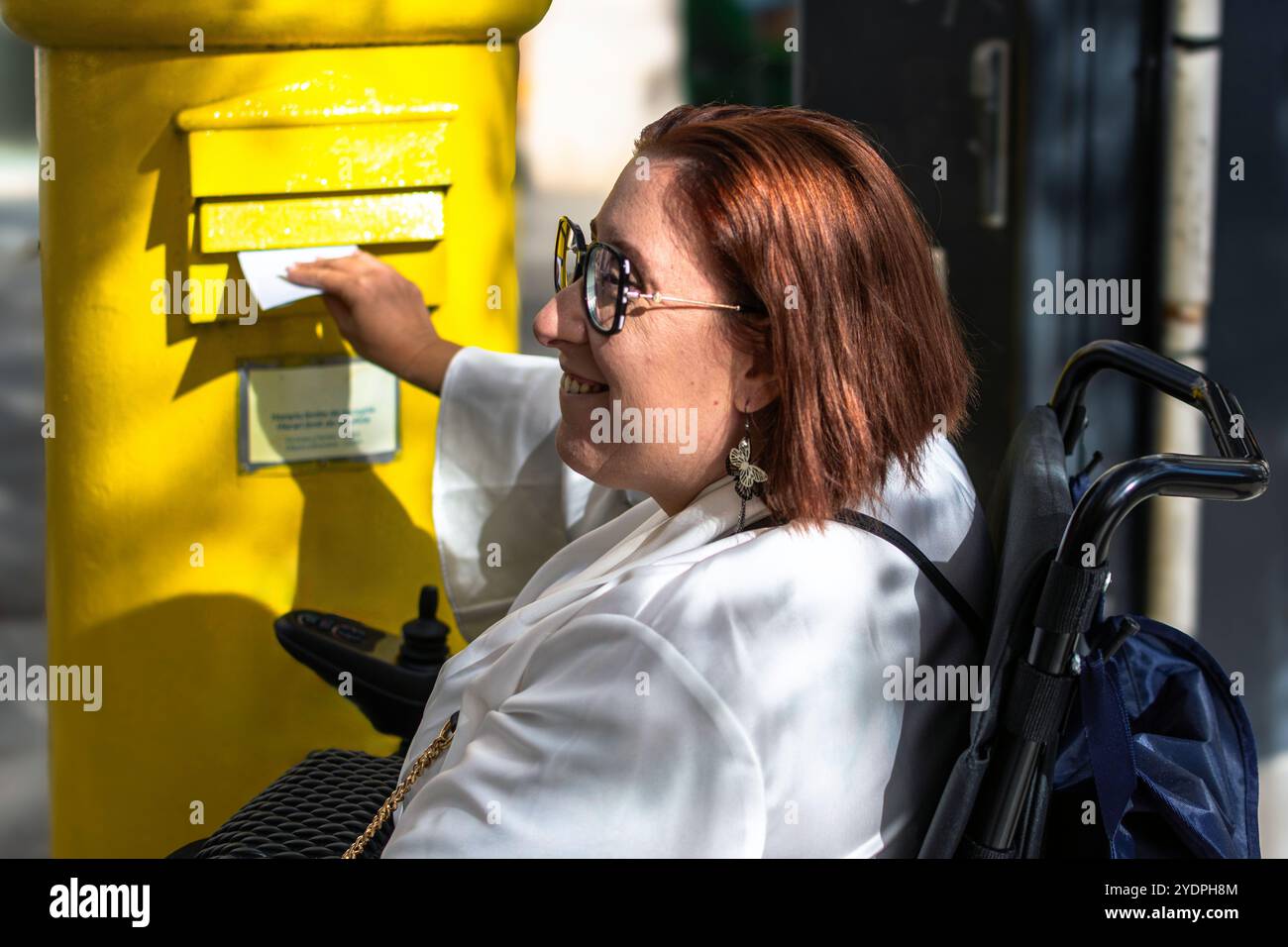 Donna sorridente in sedia a rotelle pubblicare una lettera in Yellow Mailbox Foto Stock