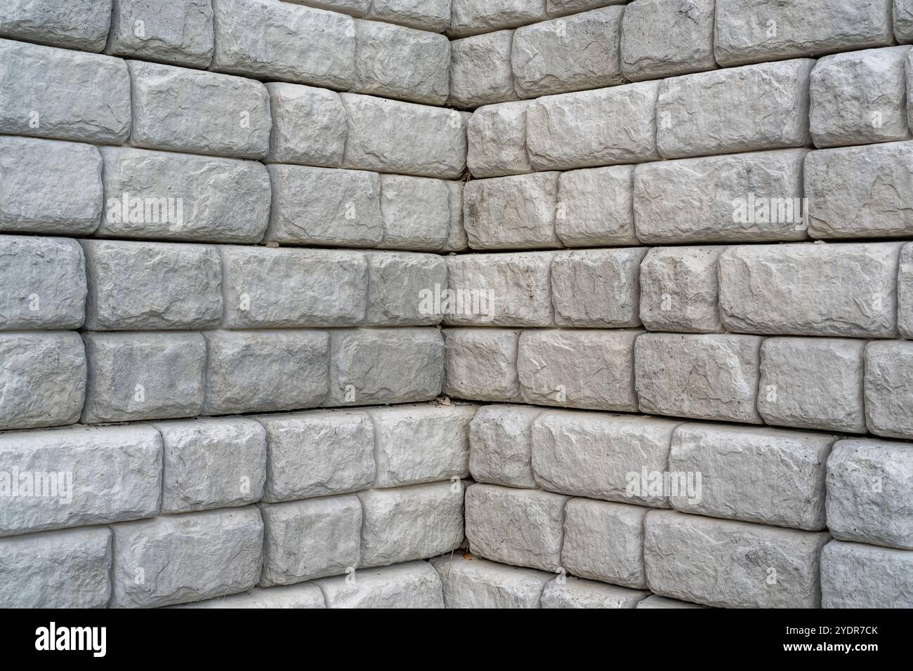 Angolo del muro di contenimento segmentato accanto a una nuova pista da running nera con linee bianche. Foto Stock