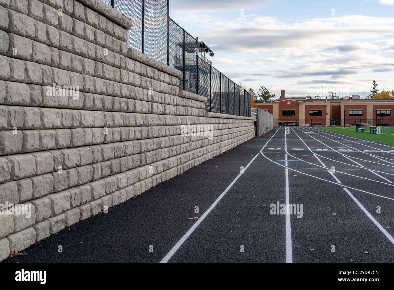Parete di contenimento segmentata accanto a una nuova pista da running nera con linee bianche. Foto Stock