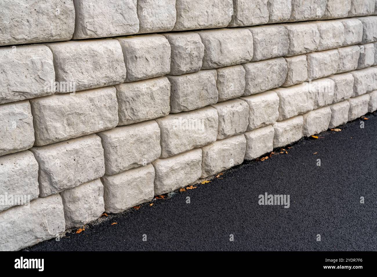 Parete di contenimento segmentata accanto a una nuova pista da running nera con linee bianche. Foto Stock